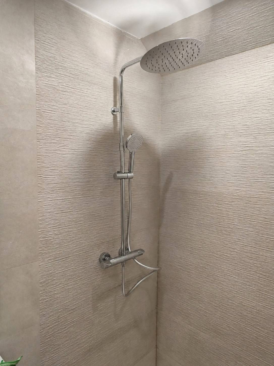 Reforma de baño con columna de ducha cromada sobre revestimiento cerámico texturizado en Alicante